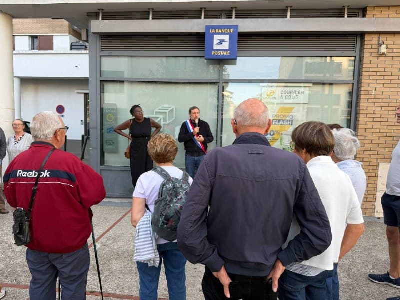 Devant l’agence de La Banque postale, un groupe d’habitants écoute l’homme au micro en écharpe tricolore.