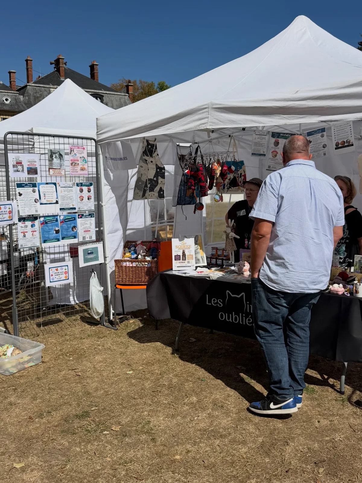 Un stand associatif sous tente blanche, avec ses panneaux d’information et sa table de présentation ; un visiteur s’y arrête.
