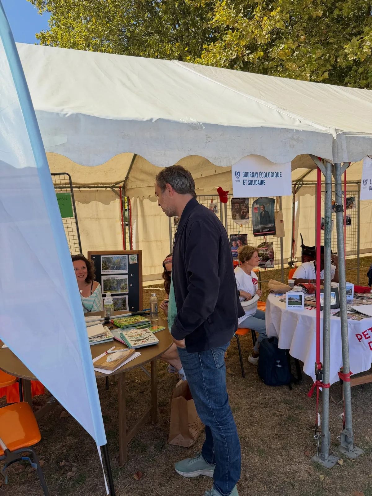 Sous un chapiteau, un visiteur regarde les documents posés sur la table d’un stand associatif.
