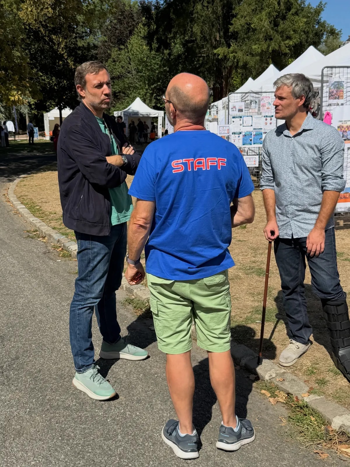 Trois hommes discutent debout dans une allée du forum, dont l’un porte un tee-shirt « Staff ».