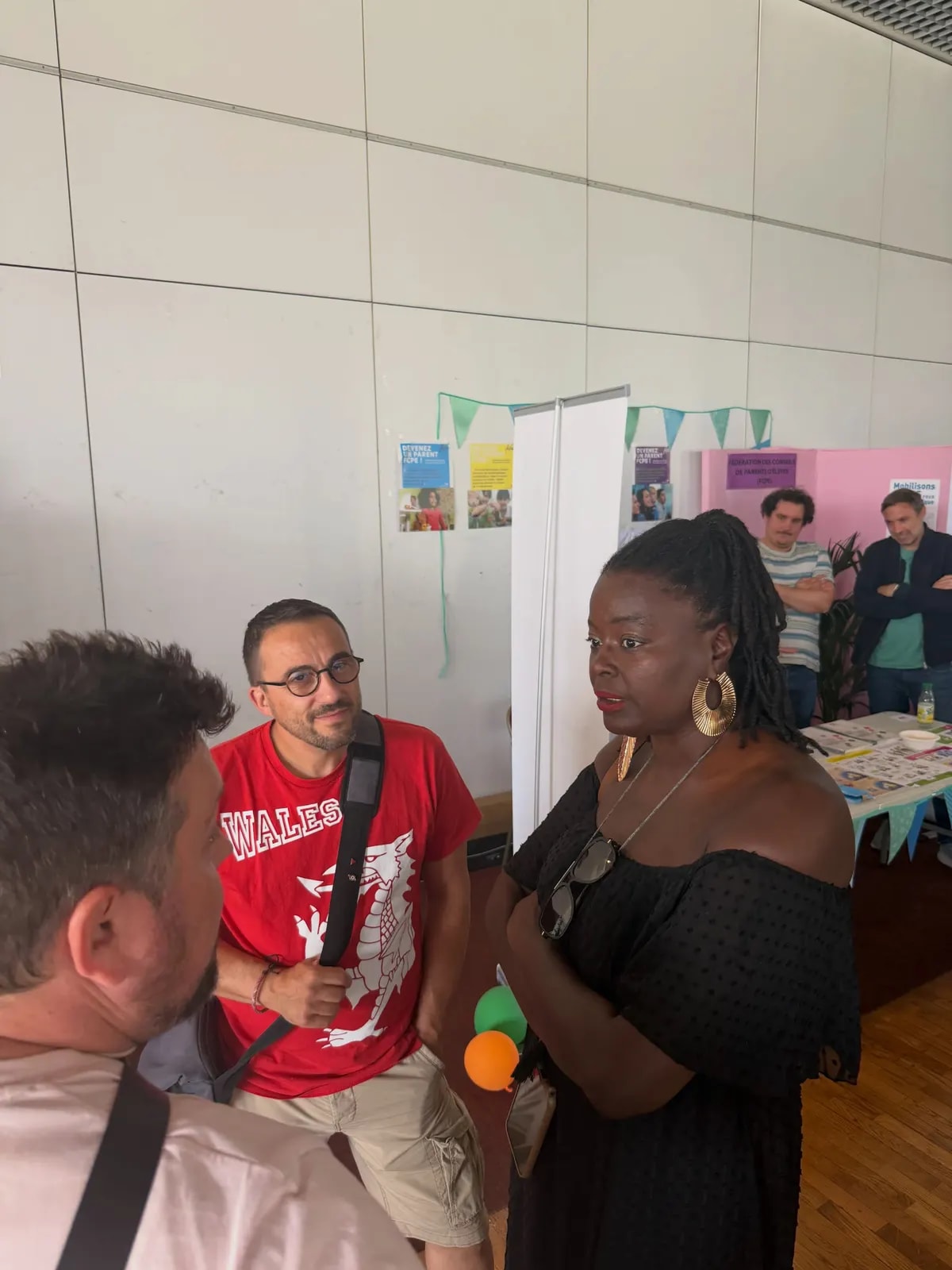Dans une salle, plusieurs personnes discutent près des stands installés le long du mur.
