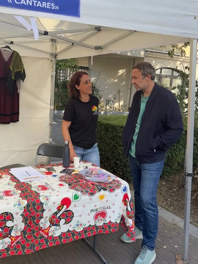 Sous une tente, deux personnes discutent devant une table couverte d’une nappe portugaise.
