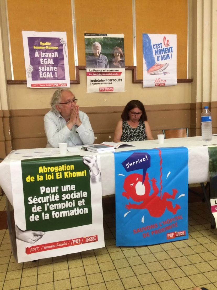 Homme et femme à une table de réunion, devant des affiches PCF et Front de gauche dont « Sauvons l'hôpital de proximité »