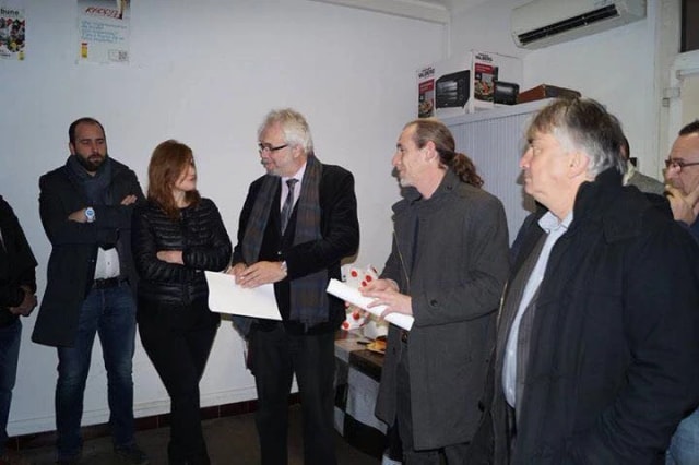 Une dizaine de personnes debout dans un local, en discussion, plusieurs tenant des documents.