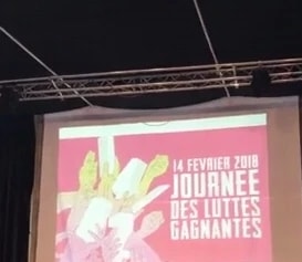 Écran de salle projetant l'affiche « Journée des luttes gagnantes » du 14 février 2018