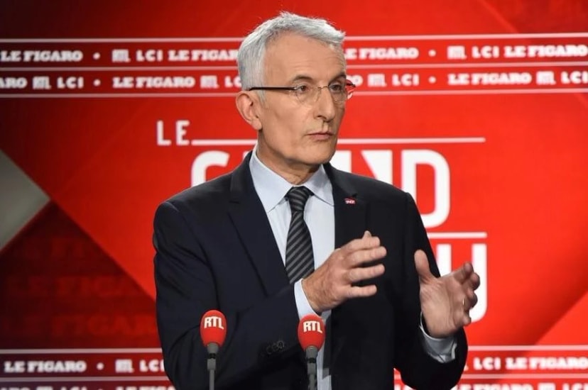 Homme aux cheveux gris en costume, parlant devant des micros RTL sur un décor rouge aux logos Le Figaro et LCI