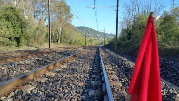 Voie ferrée unique en courbe dans une vallée boisée, un drapeau rouge planté au premier plan.