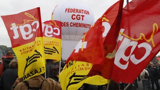 Drapeaux rouges et jaunes de la CGT-Cheminots levés dans une manifestation, un ballon gonflable au fond.
