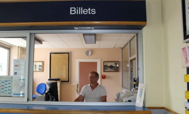 Un agent derrière le guichet « Billets » d’une petite gare.