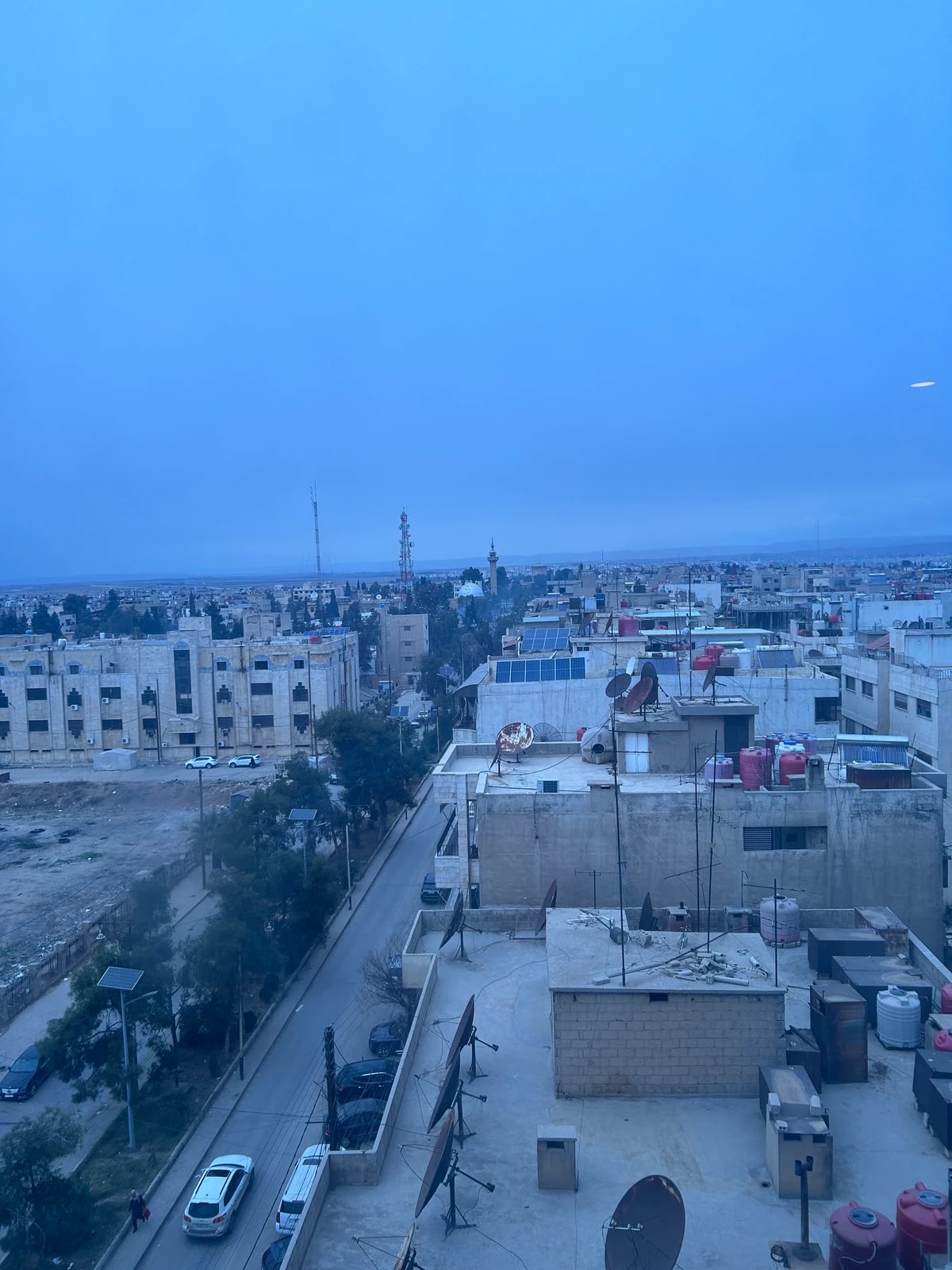 Vue d’une ville depuis un toit au petit jour, terrasses, paraboles et minaret au loin.