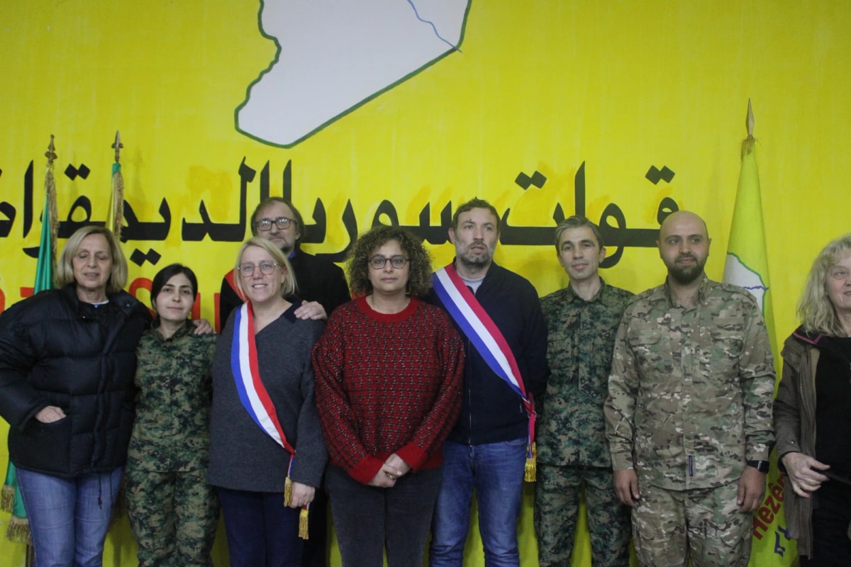 Groupe devant une banderole jaune : plusieurs personnes en écharpe tricolore aux côtés de personnes en tenue militaire.