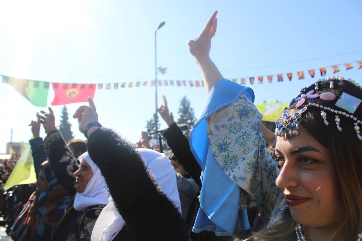Femmes en habits de fête levant la main dans une foule, guirlandes de fanions colorés au-dessus d’elles.