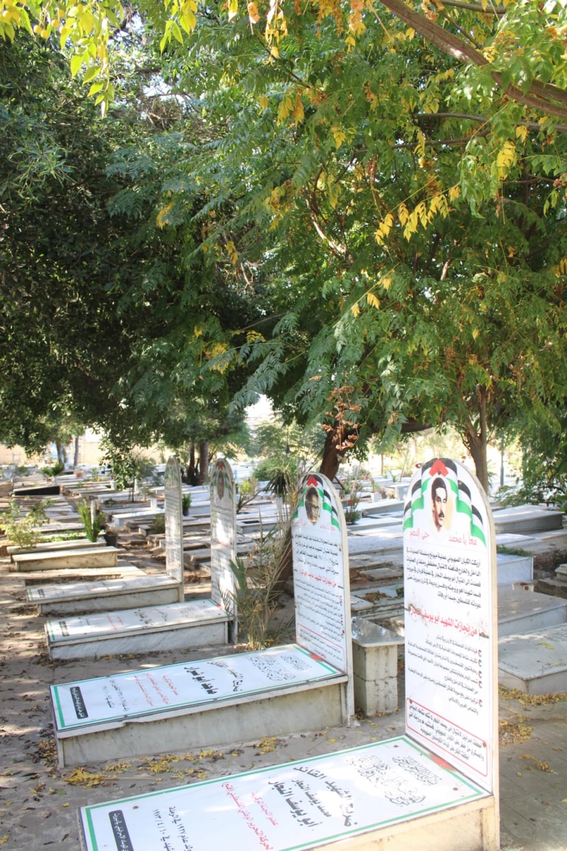 Cimetière ombragé où les stèles portent des portraits et des inscriptions en arabe.