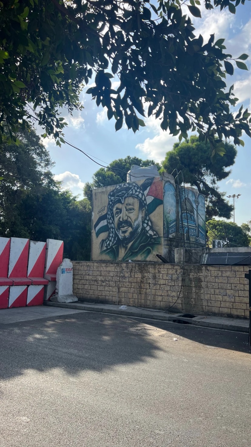 Fresque murale représentant un homme en keffieh, peinte sur un mur au-dessus d’une rue.