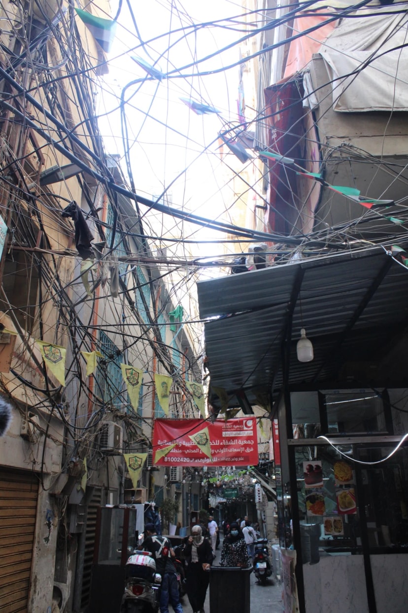 Ruelle étroite d’un quartier dense, enchevêtrement de câbles électriques au-dessus des passants.